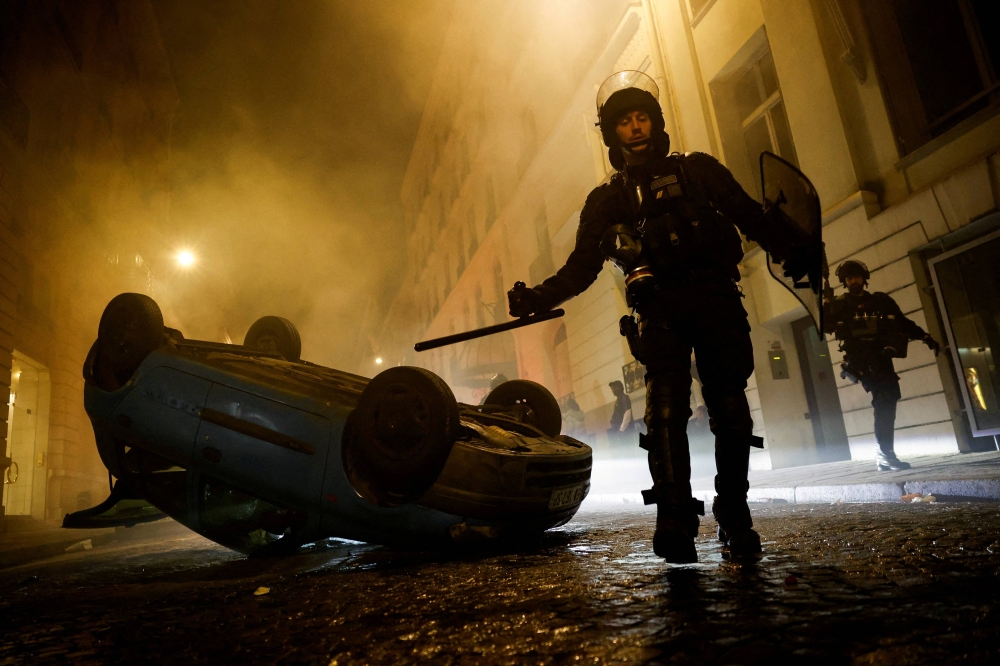 شرطي فرنسي أمام سيارة مقلوبة في نانتير ليل السبت - الأحد (رويترز)