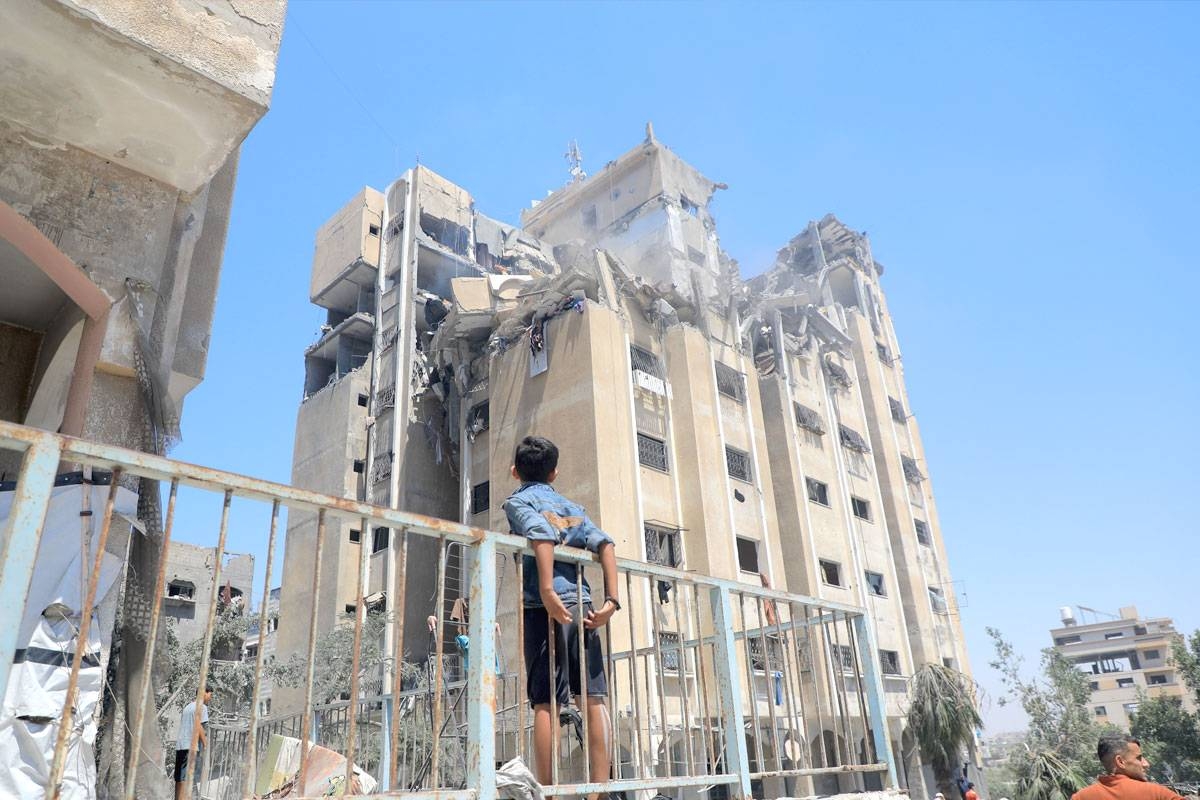 فلسطينيون بمحيط برج سكني دمرته غارة إسرائيلية في مخيم النصيرات وسط غزة أمس (شينخوا)